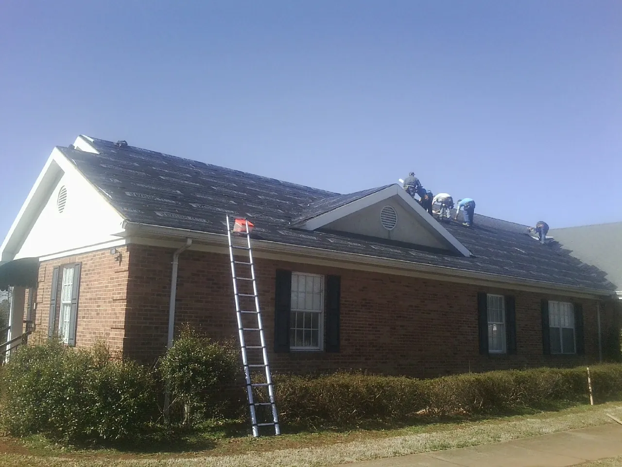 Crew tearing shingles off a brick ranch roof with a ladder set — Emergency Roof Repair work by our crew in Moore