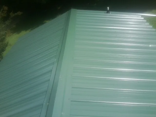 New green metal panels meeting at the ridge of a roof — Flat Roof Repair work by our crew in Moore